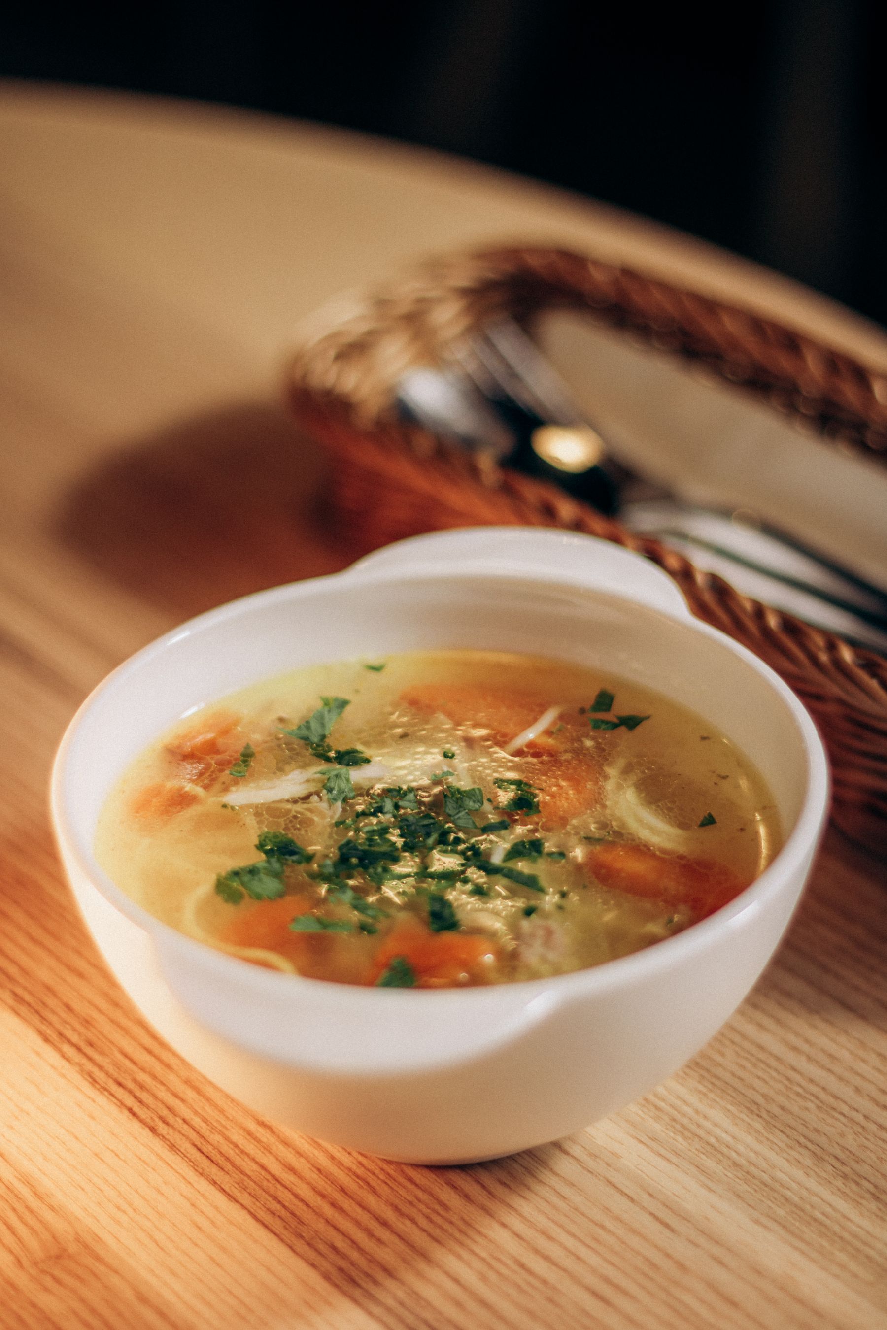 A bowl of chicken noodle soup on a wooden table, shown as a serving illustration
