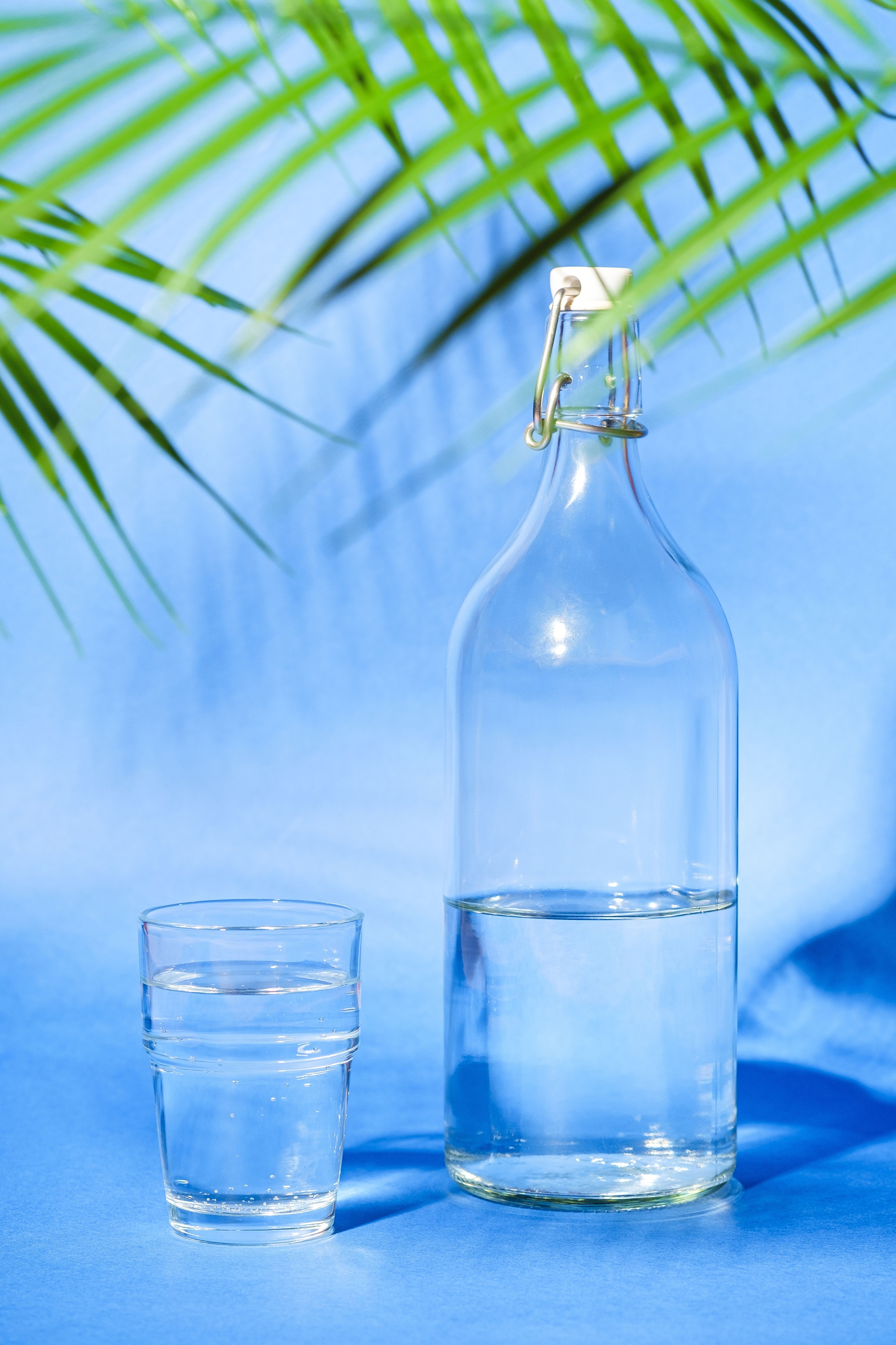 An unbranded glass water bottle and glass on a blue background, shown as a water illustration
